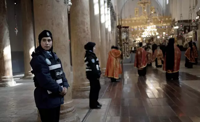 A Palestinian police woman stands guard as Greek Orthodox clergy gather in the Church of the Nativity, where Christians believe Jesus Christ was born, ahead of Christmas Eve mass in the West Bank city of Bethlehem, Monday, Jan. 6, 2025. (AP Photo/Maya Alleruzzo)