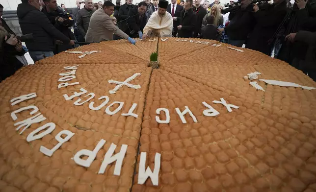 A priest, center, breaks traditional Christmas bread to mark the Orthodox Christmas Day festivities in Belgrade, Serbia, Tuesday, Jan. 7, 2025. (AP Photo/Darko Vojinovic)