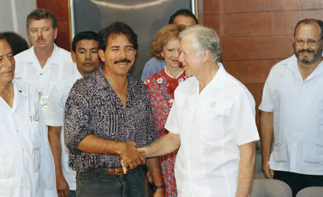 FILE - Former U.S. President Jimmy Carter, right, shakes hands with Nicaraguan President Daniel Ortega during elections in Managua, Feb. 24, 1990. In background in between Carter and Ortega is former first lady Rosalyn Carter. (AP Photo, File)