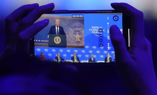 A woman takes pictures during a virtual speech of U.S. president Donald Trump at the Annual Meeting of World Economic Forum in Davos, Switzerland, Thursday, Jan. 23, 2025. (AP Photo/Markus Schreiber)
