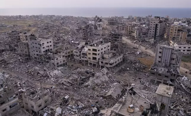 Palestinians walk through buildings that were destroyed by the Israeli air and ground offensive are seen at the Tel al-Hawa neighbourhood in Gaza Strip, Tuesday, Jan. 28, 2025. (AP Photo/Mohamamd Abu Samra)