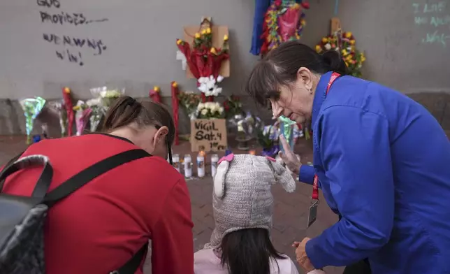 Allyson Tomkins, right, prays with Emily Lara, 5, center, and her grandmother Charity Lara, right, at a memorial to the victims of a deadly truck attack on Bourbon Street in the French Quarter, Friday, Jan. 3, 2025, in New Orleans. (AP Photo/George Walker IV)