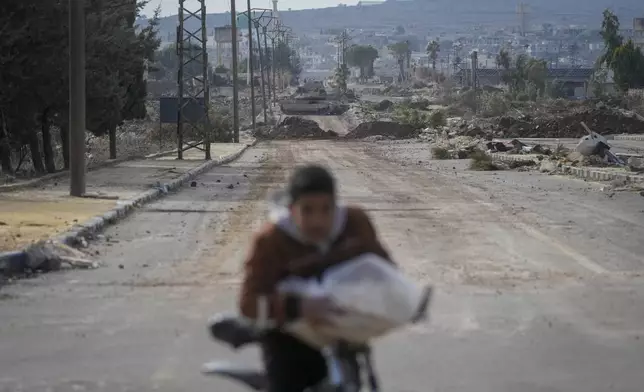 A boy rides his bicycle on a road blocked by Israeli army armoured vehicles in the outskirts of the town of Quneitra, Syria, Sunday Jan. 5, 2025.(AP Photo/Mosa'ab Elshamy)