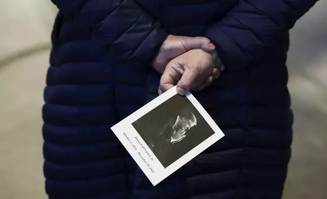 A mourner carries a picture of former President Jimmy Carter as she stands near his casket as he lies in repose at the Jimmy Carter Presidential Library and Museum in Atlanta, Monday, Jan. 6, 2025. Carter died Dec. 29 at the age of 100. (Joe Raedle/Pool via AP)