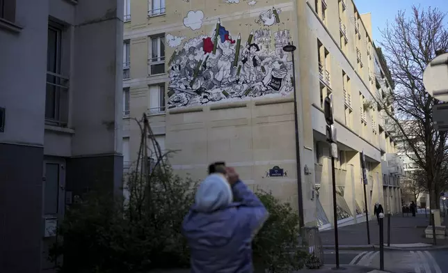 A woman takes a snapshot of a fresco by French street artist Nilko referring to the "Liberty Leading the People" painting by Eugene Delacroix during commemorations marking 10 years since an Islamist attack on the Charlie Hebdo satirical newspaper and the Hypercacher jewish supermarket, in Paris Tuesday Jan. 7, 2025. (AP Photo/Thibault Camus)