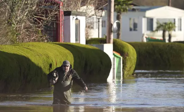 A man wearing waders carries a dog at The Little Venice caravan park, surrounded by rising flood water, in Yalding, England, Tuesday, Jan. 7, 2025, as weather warnings were issued across much of the UK. (Gareth Fuller/PA via AP)