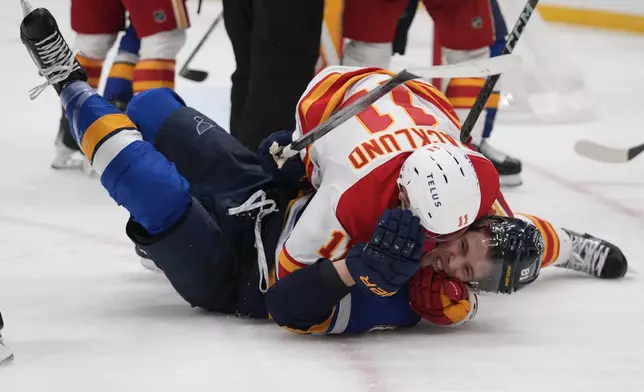 CORRECTS TO BLUES' DYLAN HOLLOWAY NOT PAVEL BUCHNEVICH - St. Louis Blues' Dylan Holloway, bottom, and Calgary Flames' Mikael Backlund (11) fight during the second period of an NHL hockey game Thursday, Jan. 16, 2025, in St. Louis. (AP Photo/Jeff Roberson)