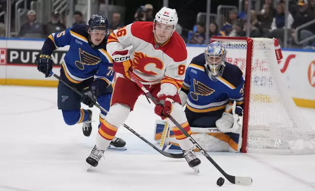 Calgary Flames' Rory Kerins (86) controls the puck as St. Louis Blues' Tyler Tucker (75) and goaltender Joel Hofer (30) defend during the first period of an NHL hockey game Thursday, Jan. 16, 2025, in St. Louis. (AP Photo/Jeff Roberson)