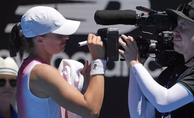 Iga Swiatek of Poland signs a screen on a television camera after defeating Emma Raducanu of Britain in their third round match at the Australian Open tennis championship in Melbourne, Australia, Saturday, Jan. 18, 2025. (AP Photo/Asanka Brendon Ratnayake)