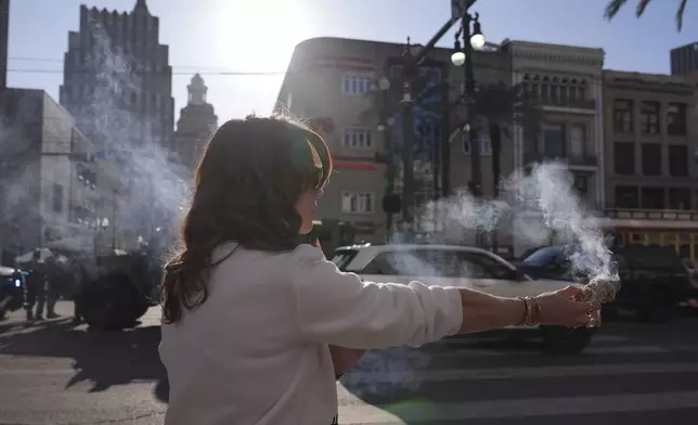 Stephanie Drake burns sage on Canal and Bourbon Street, Thursday, Jan. 2, 2025 in New Orleans. (AP Photo/George Walker IV)