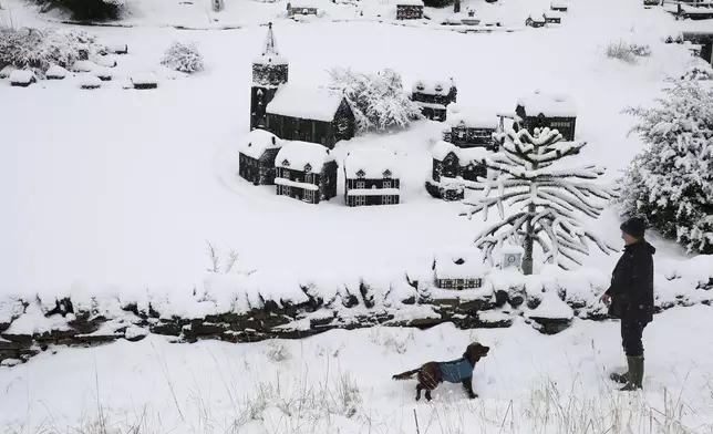 A man walk's his dog in the heavy snow past scaled miniature famous landmarks which are located in Nenthead, England, as the severe weather continues across England, Sunday, Jan. 5, 2025. (AP Photo/Scott Heppell)