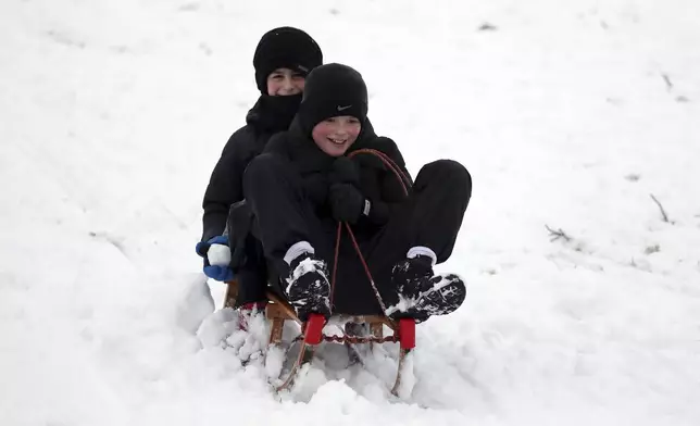 Boys are seen with a sledge on a hill with Durham Cathedral which is surrounded by heavy snow in Durham, North East England, as the severe weather continues across England, Sunday, Jan. 5, 2025. (AP Photo/Scott Heppell)