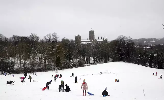 Members of the public are seen sledging on a hill with Durham Cathedral which is surrounded by heavy snow in Durham, North East England, as the severe weather continues across England, Sunday, Jan. 5, 2025. (AP Photo/Scott Heppell)