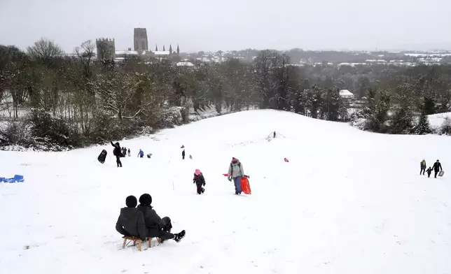 Members of the public are seen sledging on a hill with Durham Cathedral which is surrounded by heavy snow in Durham, North East England, as the severe weather continues across England, Sunday, Jan. 5, 2025. (AP Photo/Scott Heppell)