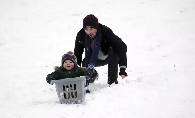 A man is seen with his son as they sledge on a hill with Durham Cathedral which is surrounded by heavy snow in Durham, North East England, as the severe weather continues across England, Sunday, Jan. 5, 2025. (AP Photo/Scott Heppell)