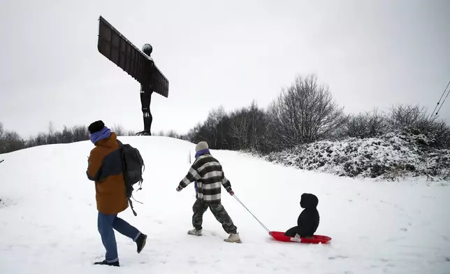 A lady is seen pulling her child along on a sledge as they admire Anthony Gormley's sculpture, the Angel of the North, which is surrounded by heavy snow in Gateshead, North East England, as the severe weather continues across England, Sunday, Jan. 5, 2025. (AP Photo/Scott Heppell)