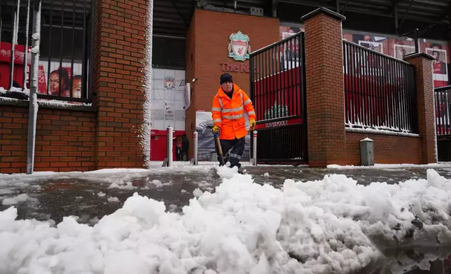 A worker clears snow from a sidewalk in front of the stadium of the premier league soccer club FC Liverpool in Liverpool, England, Sunday, Jan. 5, 2025. (Peter Byrne/PA via AP)