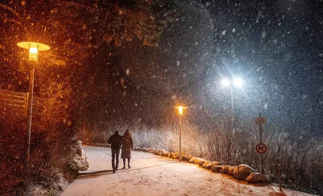 People stroll on the beach at the Baltic Sea in Timmendorfer Strand, Germany, during heavy snowfalls on Sunday, Jan. 5, 2025. (AP Photo/Michael Probst)