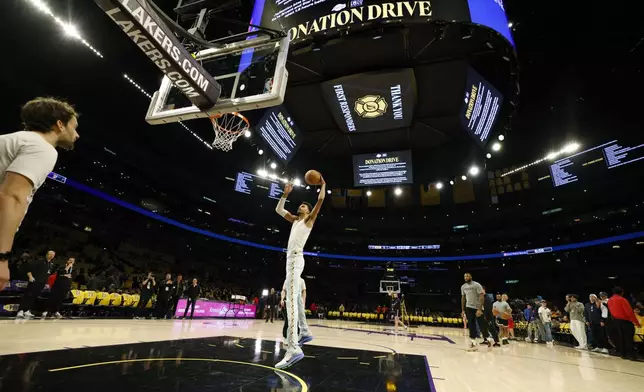 San Antonio Spurs center Victor Wembanyama, center, warms up with signs announcing the Los Angeles Lakers donation drive for California wildfires victims before an NBA basketball game Monday, Jan. 13, 2025, in Los Angeles. (AP Photo/Kevork Djansezian)
