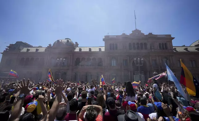 People watch Venezuela's opposition leader Edmundo Gonzalez Urrutia and Argentine President Javier Milei wave to supporters from the government house balcony in Buenos Aires, Argentina, Saturday, Jan. 4, 2025. Gonzalez, who claims he won the 2024 presidential election and is recognized by some countries as the legitimate president-elect, traveled from exile in Madrid to Argentina. (AP Photo/Natacha Pisarenko)