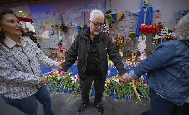 Long Island, New York residents Louis Tenedorio holds hands with family friend Angelique Whittington, left, and his wife, Cathy Tenedorio, by a memorial on Bourbon Street and Canal Street in New Orleans, Saturday, Jan. 4, 2025, where his son, Matthew Tenedorio, was killed as one of the victims of the New Year's Day deadly truck attack and shooting. (AP Photo/Matthew Hinton)