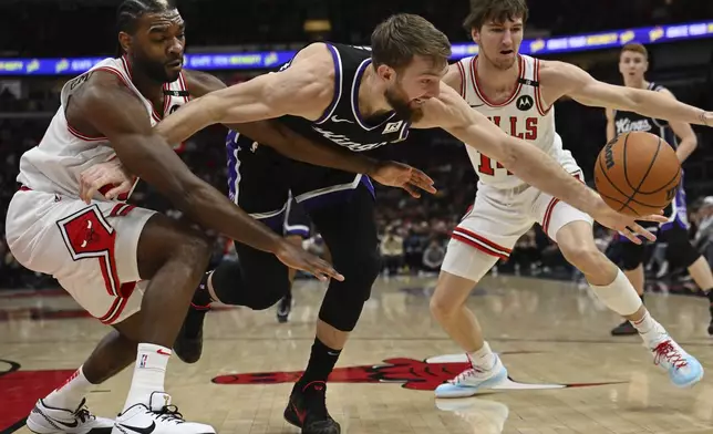 Sacramento Kings' Domantas Sabonis, center, battles against Chicago Bulls' Patrick Williams, left, and Matas Buzelis, right, for the ball during the first half of an NBA basketball game Sunday, Jan. 12, 2025, in Chicago. (AP Photo/Paul Beaty)