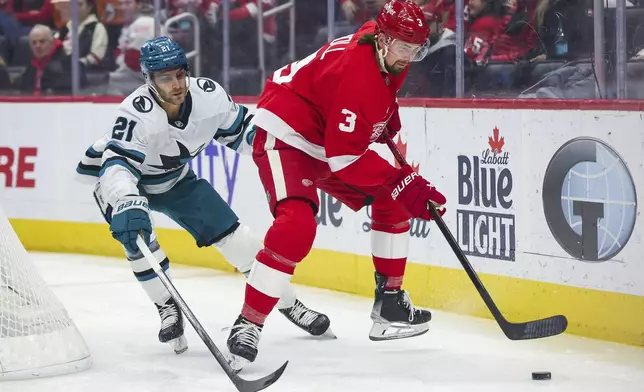 Detroit Red Wings defenseman Justin Holl (3) skates the puck out from behind the net against San Jose Sharks forward Alexander Wennberg (21) in the first period of an NHL hockey game, Tuesday, Jan. 14, 2025, in Detroit. (AP Photo/Mike Mulholland)