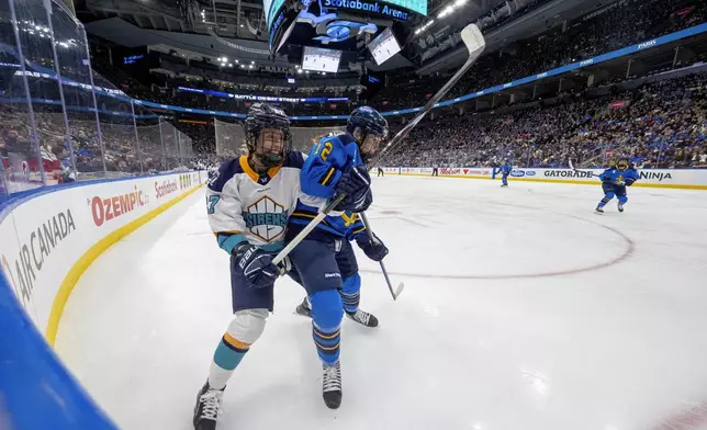 New York Sirens forward Jade Downie-Landry (27) and Toronto Sceptres defenseman Allie Munroe (12) battle for position along the boards during the second period of a PWHL hockey game in Toronto, Saturday Jan. 25, 2025. (Frank Gunn/The Canadian Press via AP)