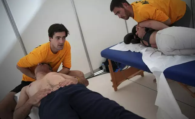 Physiotherapists treat rider Philippe Gendron, left, and co-driver Taye Perry after the ninth stage of the Dakar Rally between Riyadh and Haradh, Saudi Arabia, Tuesday, Jan. 14, 2025. (AP Photo/Christophe Ena)