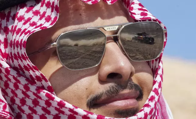 A car is reflected in the glasses of a spectator during the ninth stage of the Dakar Rally between Riyadh and Haradh, Saudi Arabia, Tuesday, Jan. 14, 2025. (AP Photo/Christophe Ena)