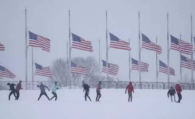 People engage in a snowball fight as U.S. flags, along the base of the Washington Monument, fly at half-staff in memorial to former President Jimmy Carter, who died at the age of 100, in Washington, Monday, Jan. 6, 2025. (AP Photo/Matt Rourke)