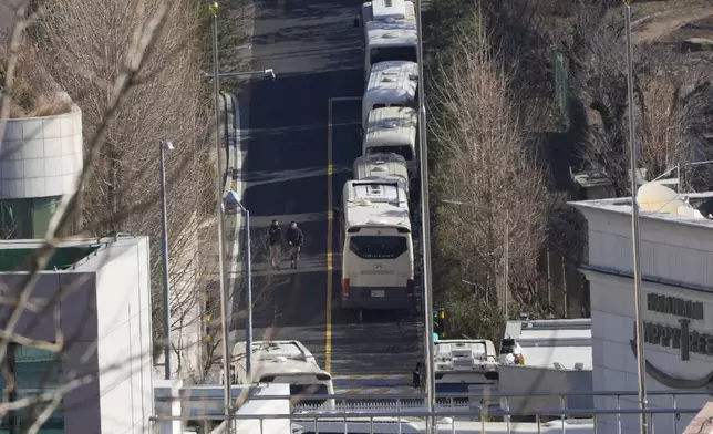 Security personnel walk on a road lined up with buses blocking the entrance gate of impeached South Korean President Yoon Suk Yeol's residence in Seoul, South Korea, Friday, Jan. 10, 2025. (AP Photo/Ahn Young-joon)