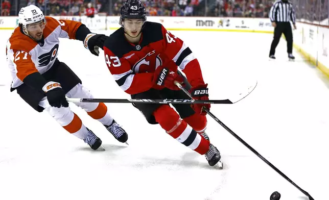 New Jersey Devils defenseman Luke Hughes (43) plays the puck ahead Philadelphia Flyers left wing Noah Cates (27)during the second period of an NHL hockey game, Saturday, Jan. 18, 2025, in Newark, N.J. (AP Photo/Noah K. Murray)