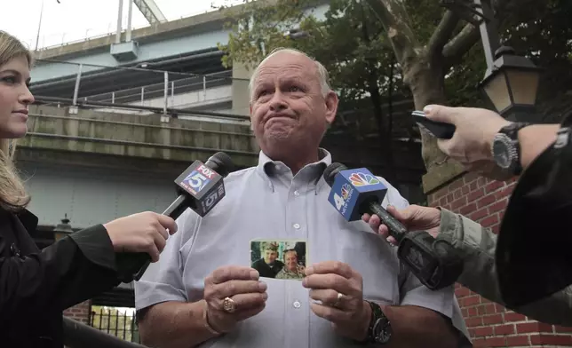 FILE - Ken Fairben holds a photo showing his son Keith, left, a victim of the Sept, 11, attacks, as he talks with reporters Oct. 15, 2012, outside Fort Hamilton Army base in Brooklyn, N.Y. (AP Photo/Bebeto Matthews, File)