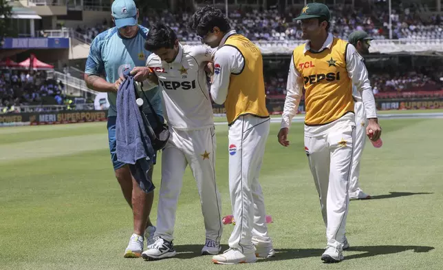 Pakistan's Saim Ayub is helped from the field after injuring his ankle while fielding the ball during the second test match between South Africa and Pakistan in Cape Town, South Africa, Friday, Jan. 3, 2025. (AP Photo/Halden Krog)