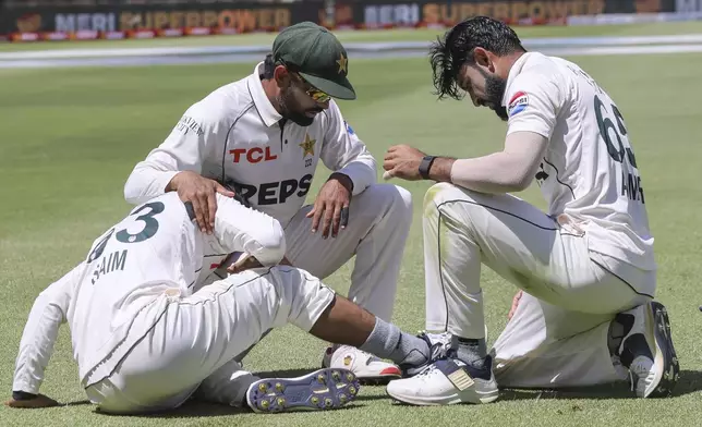 Pakistan's Saim Ayub, left, injures his ankle as Babar Azam and Aamir Jamal show concern during the second test match between South Africa and Pakistan in Cape Town, South Africa, Friday, Jan. 3, 2025. (AP Photo/Halden Krog)