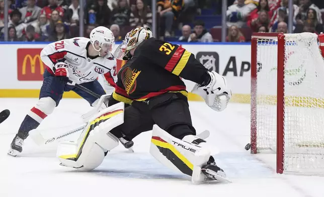 The puck hits the post behind Vancouver Canucks goalie Kevin Lankinen (32) and stays out of the net as Washington Capitals' Lars Eller (20) tries to reach for it during the first period of an NHL hockey game in Vancouver, Saturday, Jan. 25, 2025. (Darryl Dyck/The Canadian Press via AP)