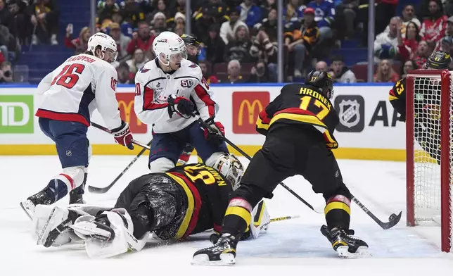 Vancouver Canucks' Filip Hronek stops the puck from entering the net behind goalie Kevin Lankinen as Washington Capitals' Lars Eller and Taylor Raddysh (16) watch during the first period of an NHL hockey game in Vancouver, British Columbia, on Saturday, Jan. 25, 2025. (Darryl Dyck/The Canadian Press via AP)