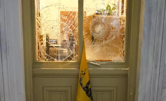 FILE - A flag hangs between broken windows after then-President Donald Trump supporters tried to break through police barriers outside the U.S. Capitol, Jan 6, 2021. (AP Photo/John Minchillo, File)