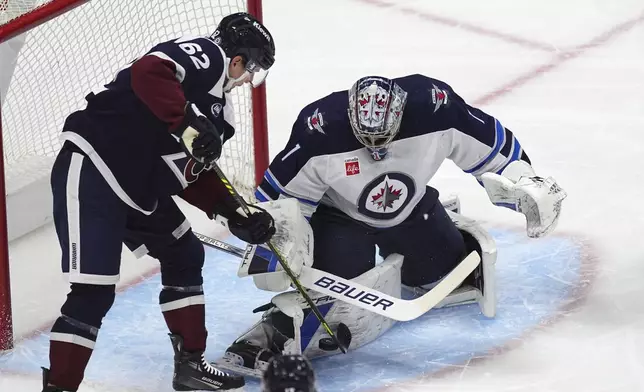 Winnipeg Jets goaltender Eric Comrie, right, stops a redirected shot by Colorado Avalanche left wing Artturi Lehkonen in the first period of an NHL hockey game Tuesday, Dec. 31, 2024, in Denver. (AP Photo/David Zalubowski)