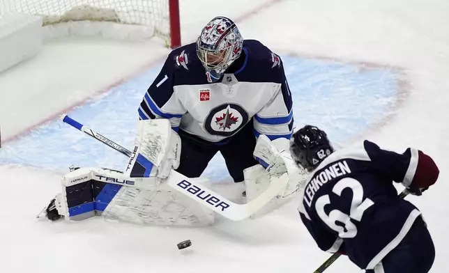 Winnipeg Jets goaltender Eric Comrie, back, makes a pad save of a shot from Colorado Avalanche left wing Artturi Lehkonen in the first period of an NHL hockey game Tuesday, Dec. 31, 2024, in Denver. (AP Photo/David Zalubowski)