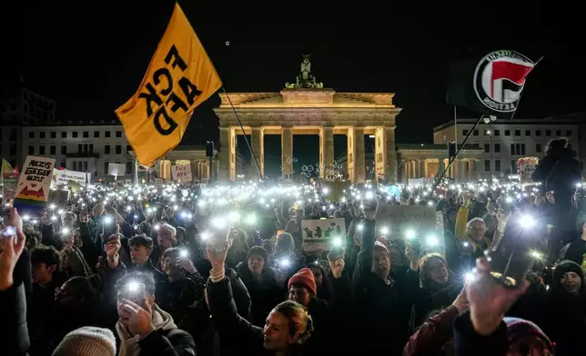 People hold up their cell phones as they protest the far-right Alternative for Germany, or AfD party, and right-wing extremism in front of the Brandenburg Gate in Berlin, Germany, Saturday, Jan. 25, 2025. (AP Photo/Ebrahim Noroozi)