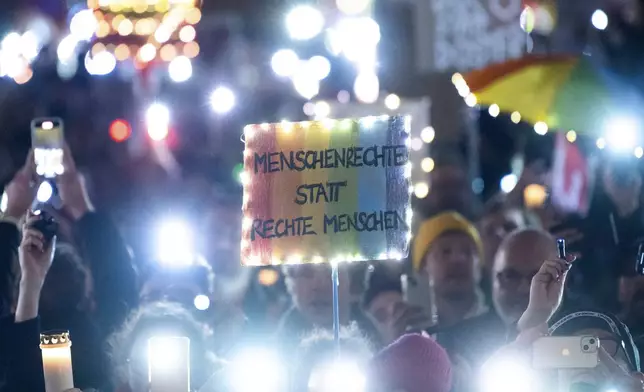 Participants hold lights, and a banner reading 'human rights instead of right people' during a rally, in front of the Brandenburg Gate, in Berlin, Saturday, Jan. 25, 2025. (Christophe Gateau/dpa via AP)