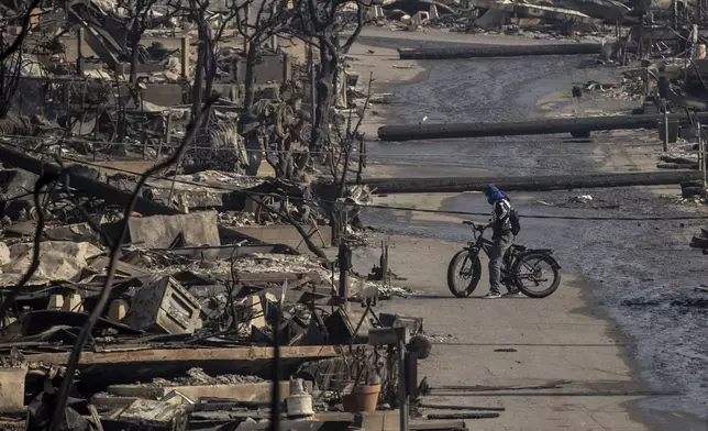 A bicyclist stands amongst Pacific Palisades Bowl Mobile Estates destroyed by the Palisades Fire in Pacific Palisades, Calif., Thursday, Jan. 9, 2025.(Stephen Lam/San Francisco Chronicle via AP)