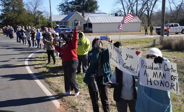 People watch as the hearse containing the flag-draped casket of former President Jimmy Carter departs the Jimmy Carter Boyhood Farm in Archery, Ga., Saturday, Jan. 4, 2025. Carter died Dec. 29 at the age of 100. (AP Photo/Alex Brandon, Pool)