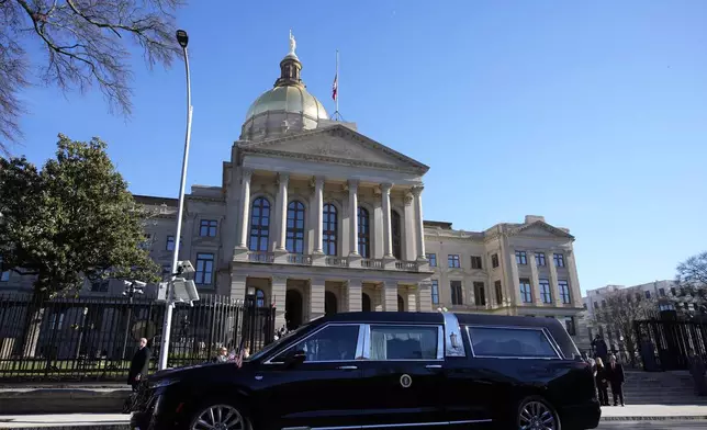 The hearse carrying the flag-draped casket of former President Jimmy Carter pauses outside the State Capitol in Atlanta, Saturday, Jan. 4, 2025. Carter died Dec. 29 at the age of 100. (AP Photo/Alex Brandon, Pool)