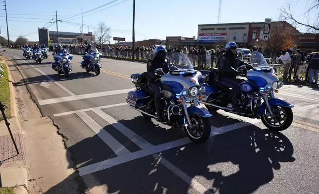 A police escort passes as the hearse carrying the flag-draped casket of former President Jimmy Carter approaches during a procession in downtown Plains, Ga., Saturday, Jan. 4, 2025. (AP Photo/Mike Stewart)