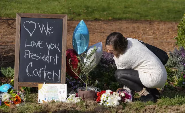 A woman leaves flowers in tribute to former President Jimmy Carter at the entrance to the Jimmy Carter Presidential Center Tuesday, Dec. 31, 2024, in Atlanta. Carter died Sunday at he age of 100. (AP Photo/John Bazemore )