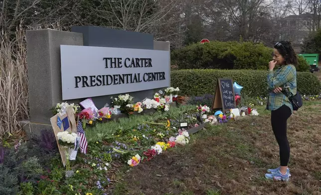 A woman looks at items left in tribute to former President Jimmy Carter at the entrance to the Jimmy Carter Presidential Center Tuesday, Dec. 31, 2024, in Atlanta. Carter died Sunday at he age of 100. (AP Photo/John Bazemore )