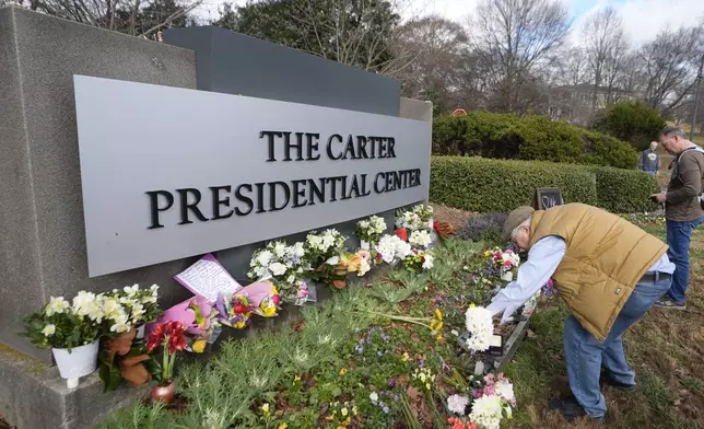 Tom Chaffin, of Atlanta, leaves flowers at the entrance to the Jimmy Carter Presidential Center Tuesday, Dec. 31, 2024, in Atlanta. Carter died Sunday at he age of 100. (AP Photo/John Bazemore )